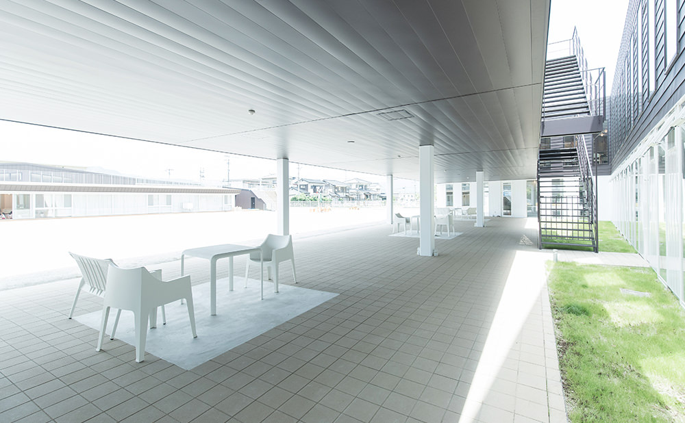 施設の屋根付き外部テラス・中庭。ベンチと椅子が配置された広々とした共用スペース。